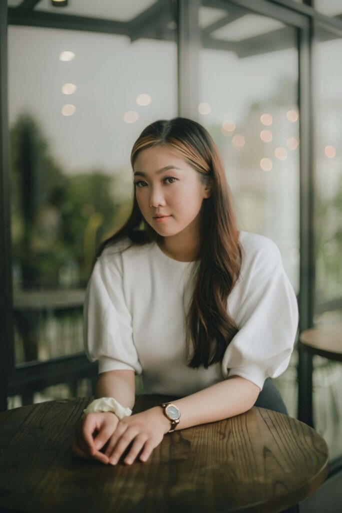 Young woman in white shirt sitting at wooden table by large windows with blurred city lights in background